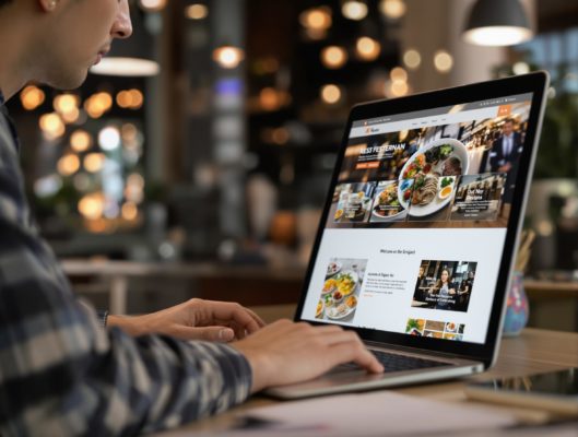 Personne utilisant un ordinateur portable affichant le site Web du restaurant KFots, avec des images de plats et des informations sur le restaurant.